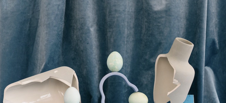Broken vases in front of a blue velvet curtain with egg-like art pieces
