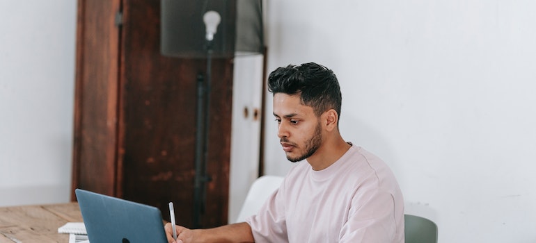 A man writing something and looking at a laptop