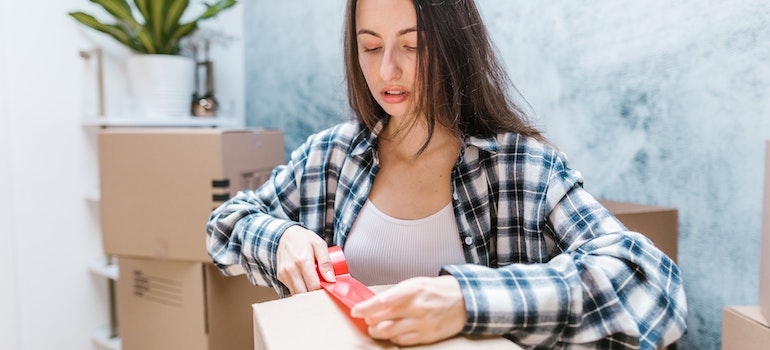 Woman being stressed, packing a cardboard box and securing it with red tape