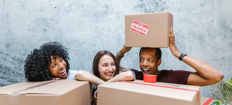 Three people smiling and holding moving boxes