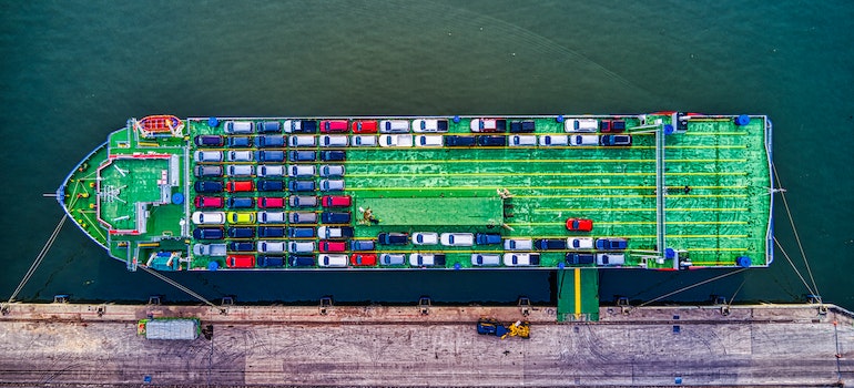 A green cargo ship docked with lots of parked cars to be transported