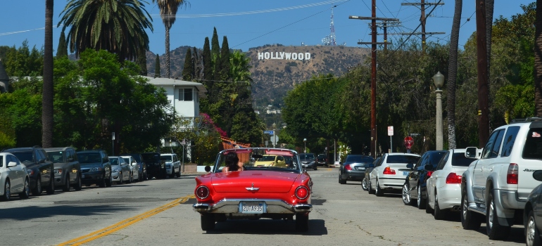 Red car on the road and the Hollywood sign in the distance