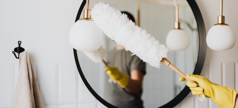 A woman using a white duster with an eco-friendly handle to clean a bathroom mirror