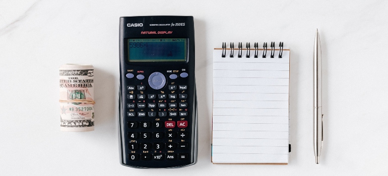 A dollar bill, calculator, and pen and paper on a table