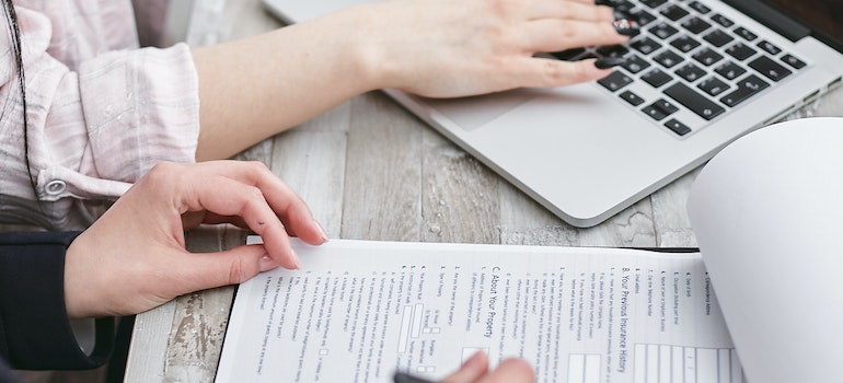 One woman using a laptop, the other taking notes in an office