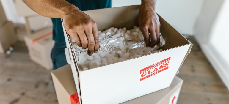 A man packing glasses in a moving box that's labelled as fragile