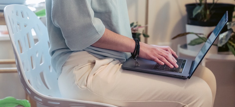 A person sitting on a white chair holding a laptop in their lap