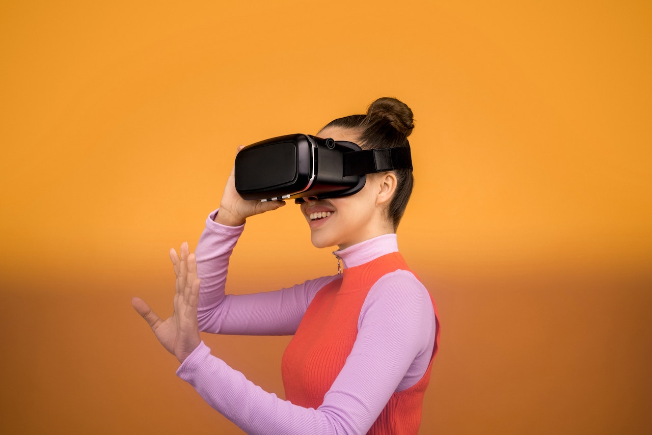 A woman with a ballerina bun wearing a purple turtleneck and an orange vest using VR glasses
