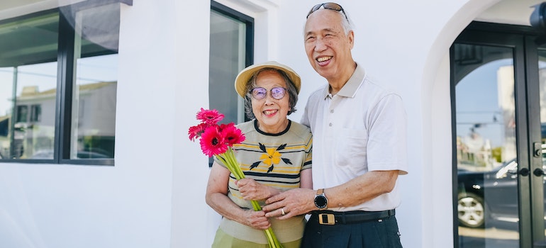 A couple in front of a house with a woman holding flowers