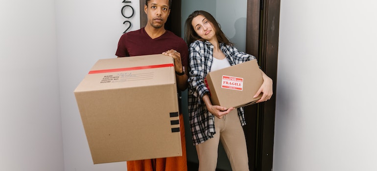A couple carrying cardboard boxes in front of doors