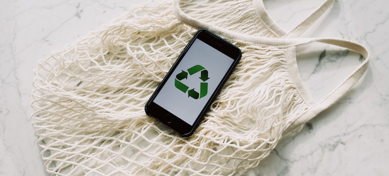 a mesh tote bag under a phone with an edo-friendly green recycling sign