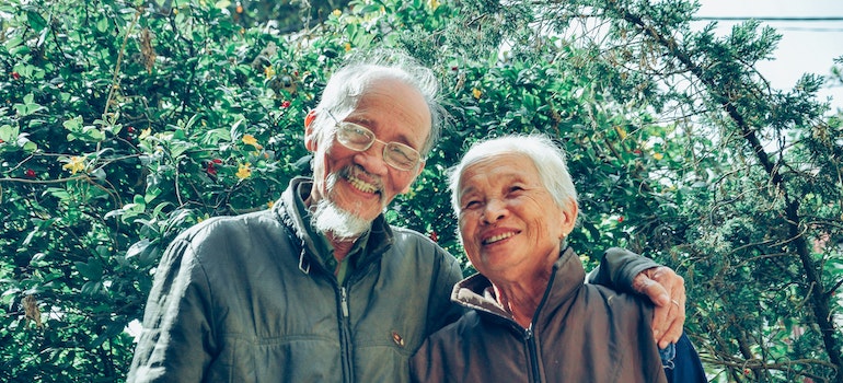 An elderly couple hugging in front of a tree