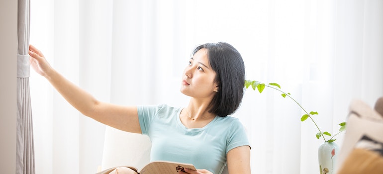 a woman sitting in her living room reading and looking and grey curtains