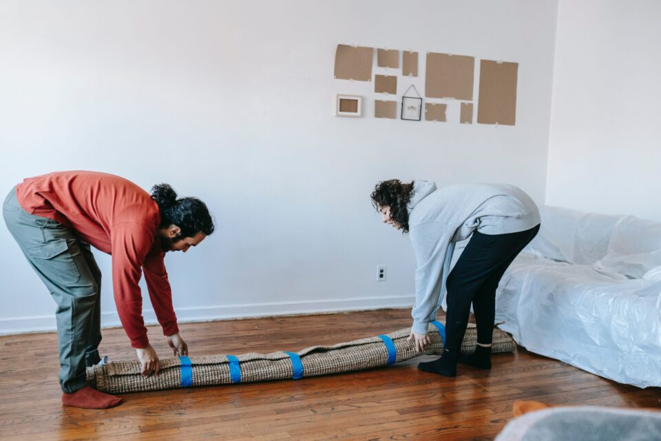 Two people putting down a wrapped up carpet