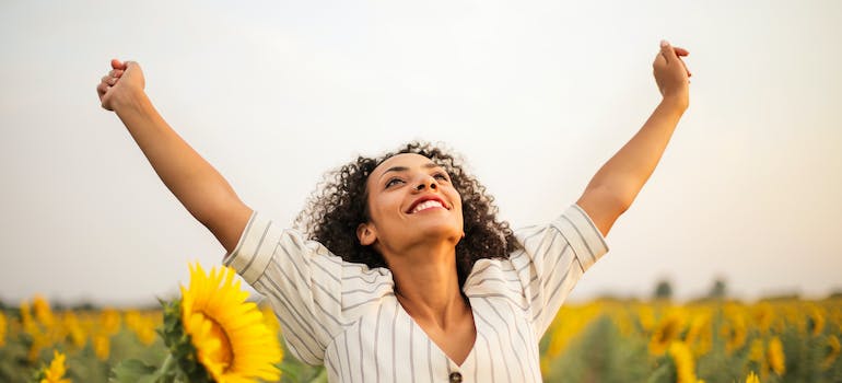 woman standing on sunflower field with hands up