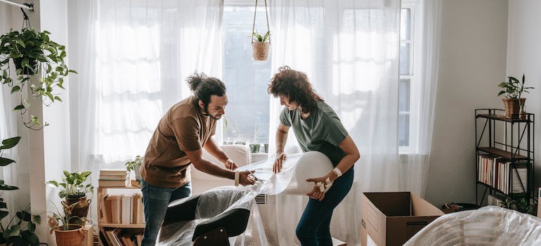 a woman and a man wrapping up a chair with bubble wrap