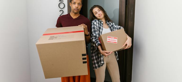 a man and a woman standing and holding moving boxes
