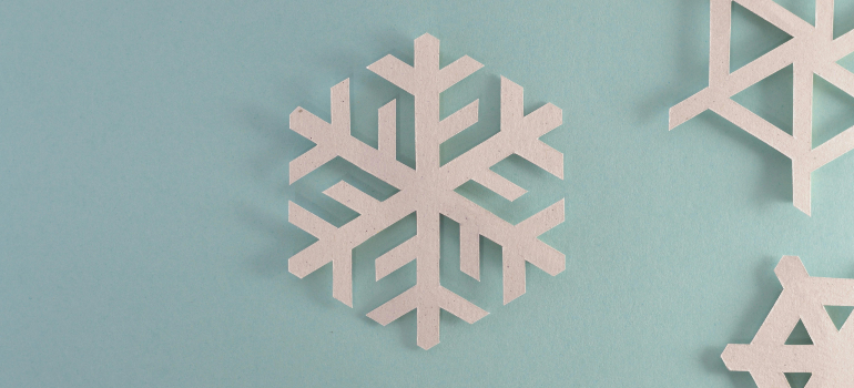 A paper snowflake cutout on a light blue background, surrounded by additional snowflake cutouts.