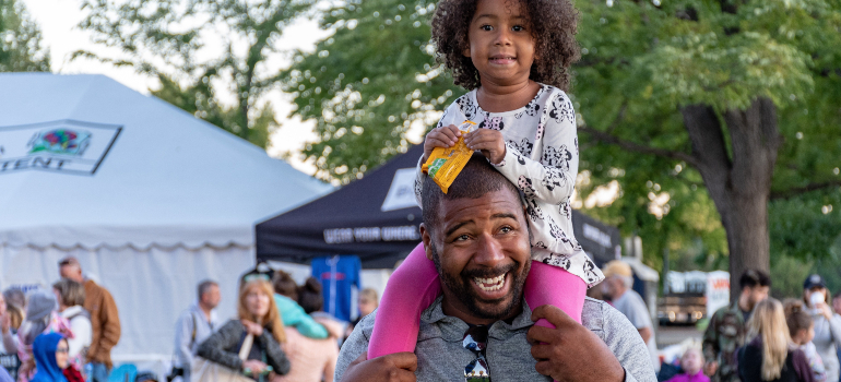 A man carrying his daughter on a local festival, representing Frederick a place for families in Maryland.