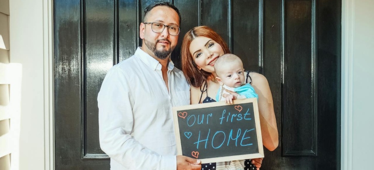 couple with their baby holding a inscription our first home' after they moved to one of the top places for families in Utah