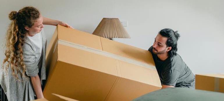 A couple trying to avoid one of the top 10 moving mistakes by carefully handling a big moving box