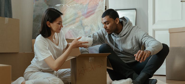 A couple packing a box and talking about what to do while movers are moving their stuff.