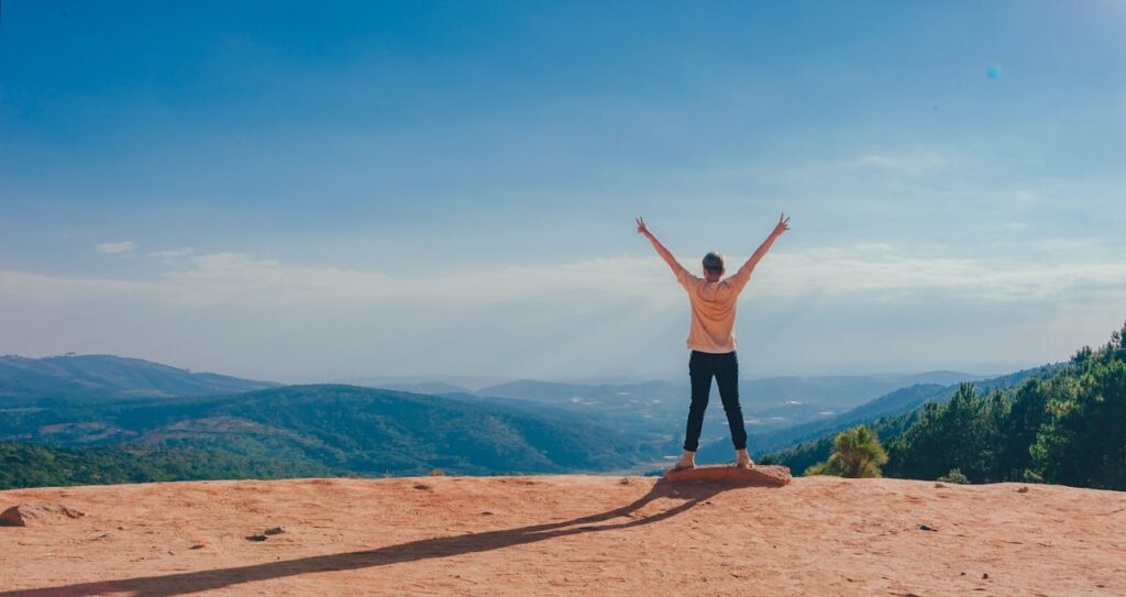 person standing on a cliff with hands up