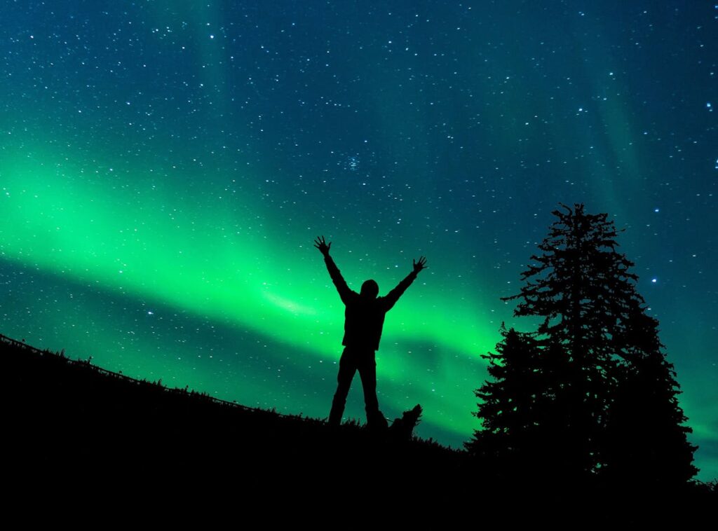 man standing with hands up and watching Aurora Borealis