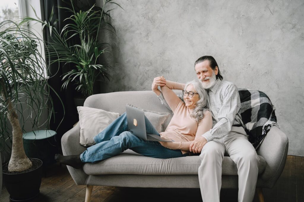 an elderly couple sitting on a couch with laptop