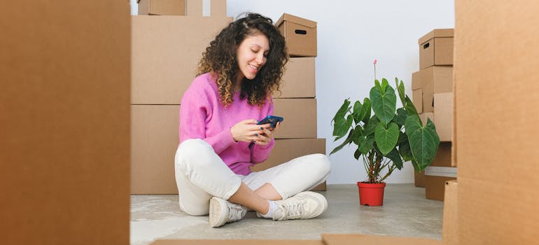 woman sitting among moving boxes and looking at her smartphone