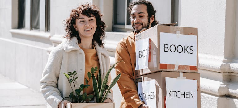 a couple carrying boxes and a plant to their new home