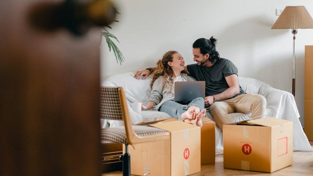 a couple sitting with laptop and having fun among boxes