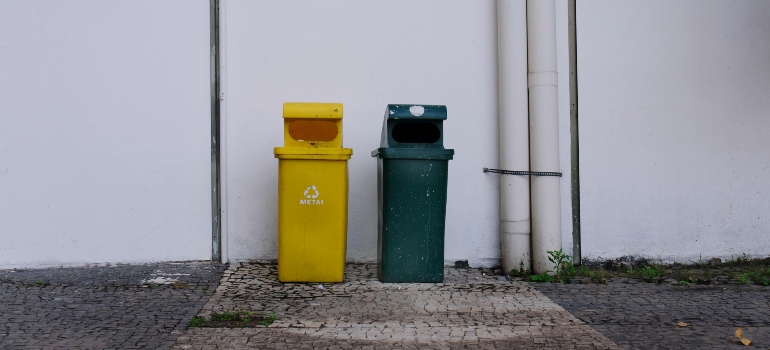 Yellow and green recycling bins against a white wall.
