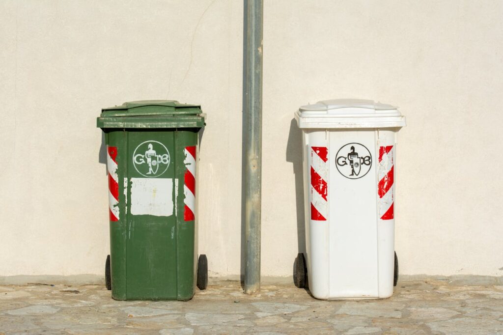 A Green and White Trashcans Standing next to a Wall of a Building
