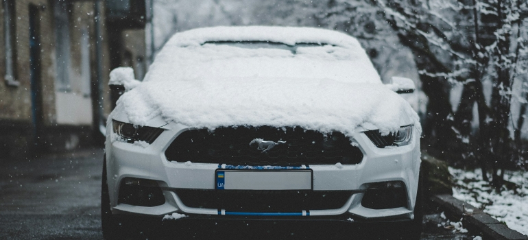 A white Ford Mustang is covered with snow. 