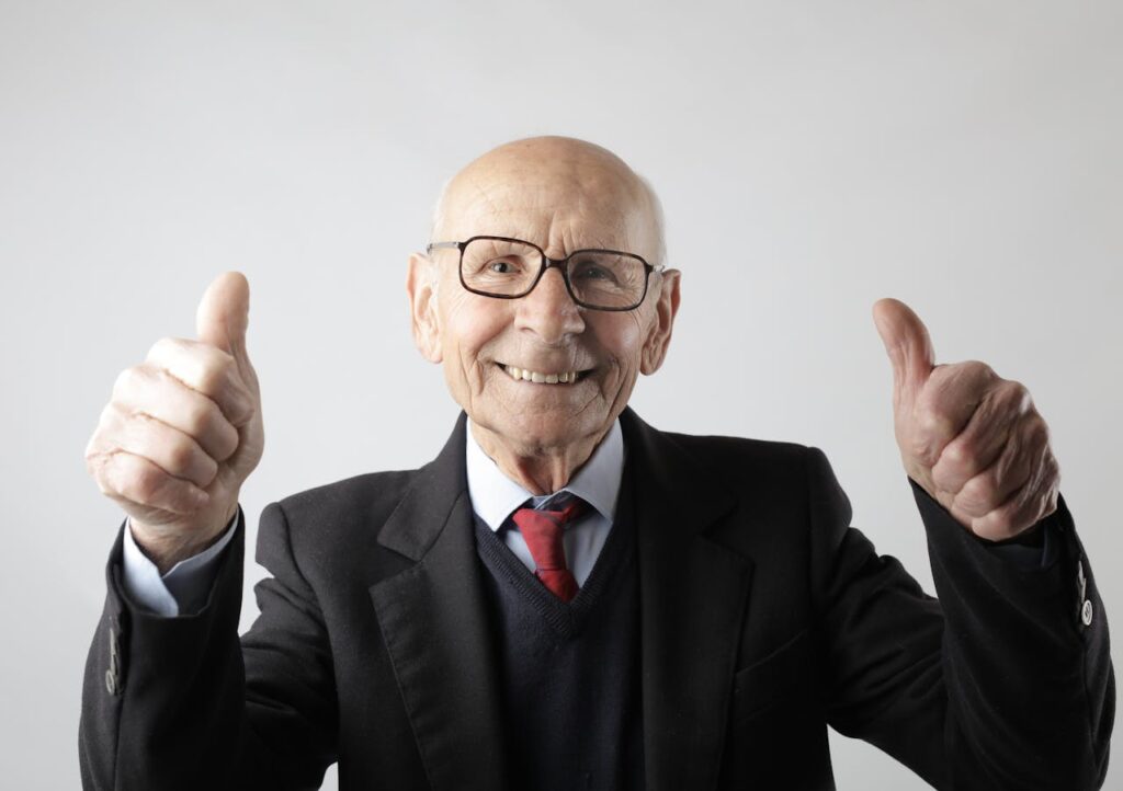 Positive senior man in eyeglasses showing thumbs up and looking at camera
