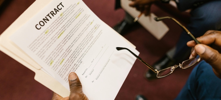 the man is holding glasses and reading the contract about shipping a car from New Jersey to Texas