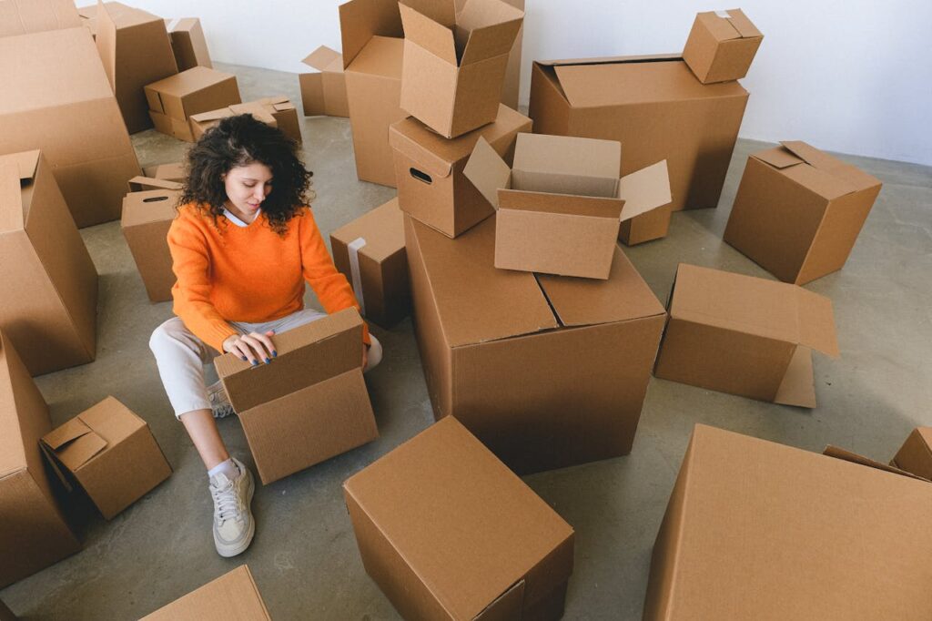 Young relocating lady packing carton boxes sitting on floor
