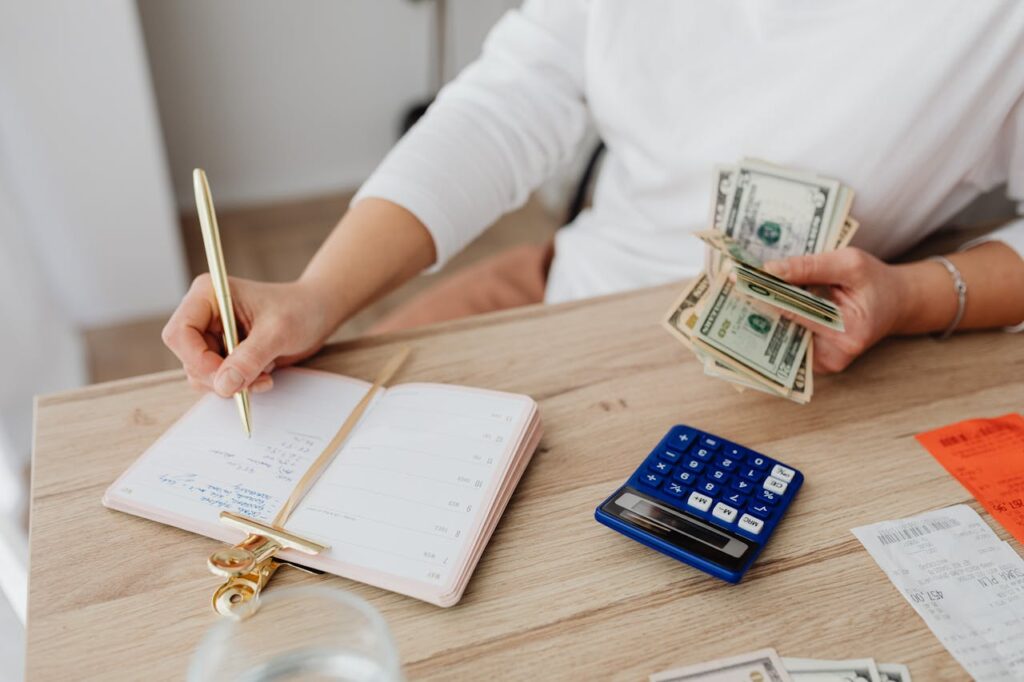 Person Writing on a Notebook while Holding Money
