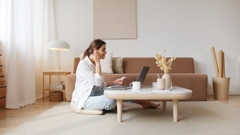 Cheerful woman with earbuds listening to music and using laptop and trying to think about the things to consider when moving abroad