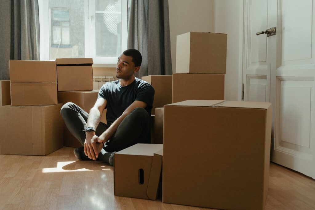 Man in Blue Crew Neck T-shirt Sitting on Brown Cardboard Box
