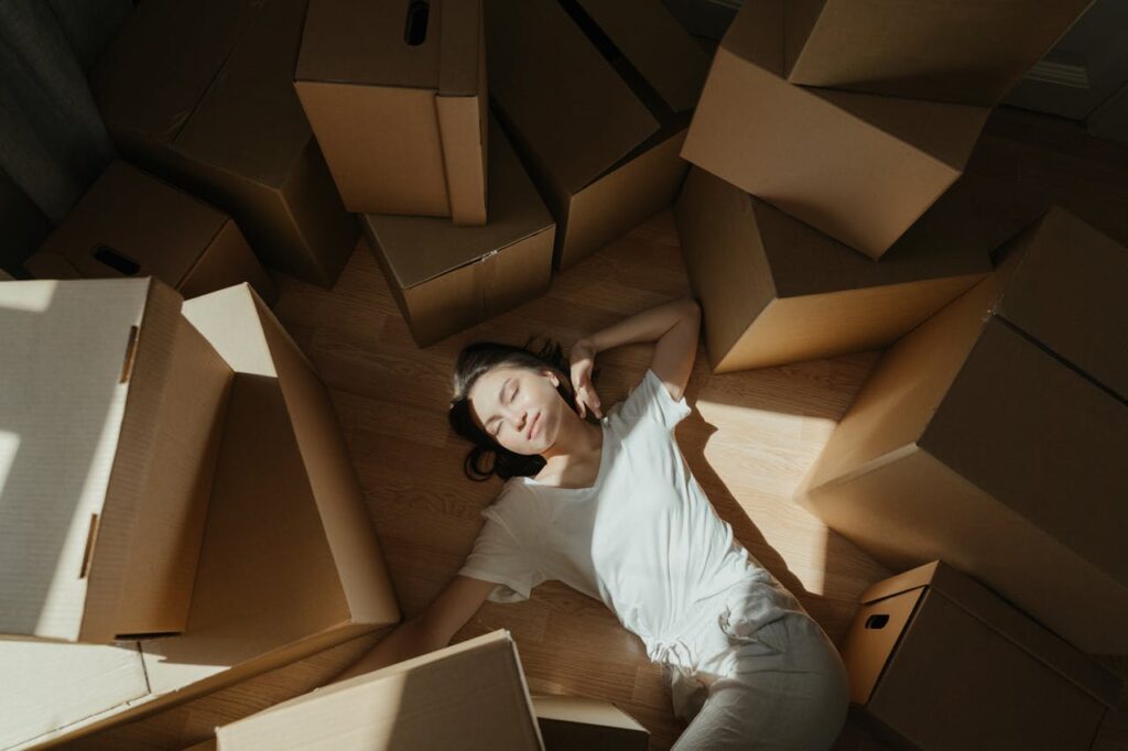 Woman in White Long Sleeve Shirt Lying on Brown Cardboard Box
