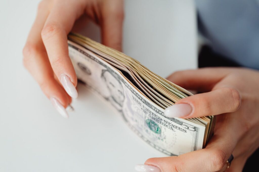 Close-Up Shot of a Person Holding Paper Money on White Surface