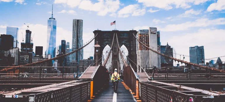 A man walking across the Brooklyn Bridge toward the Manhattan skyline